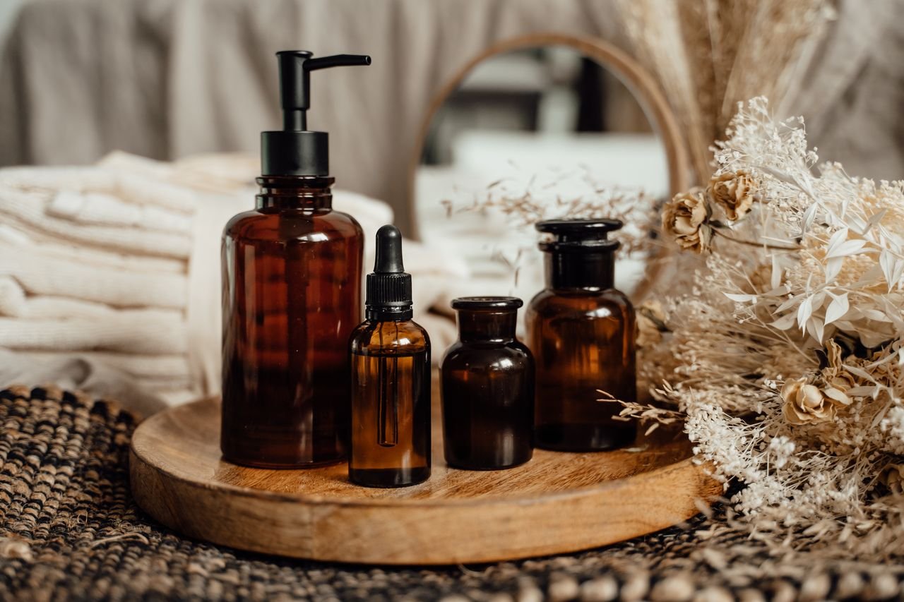 Stylish skincare setup featuring glass bottles on a wooden tray with dried flowers and towels.